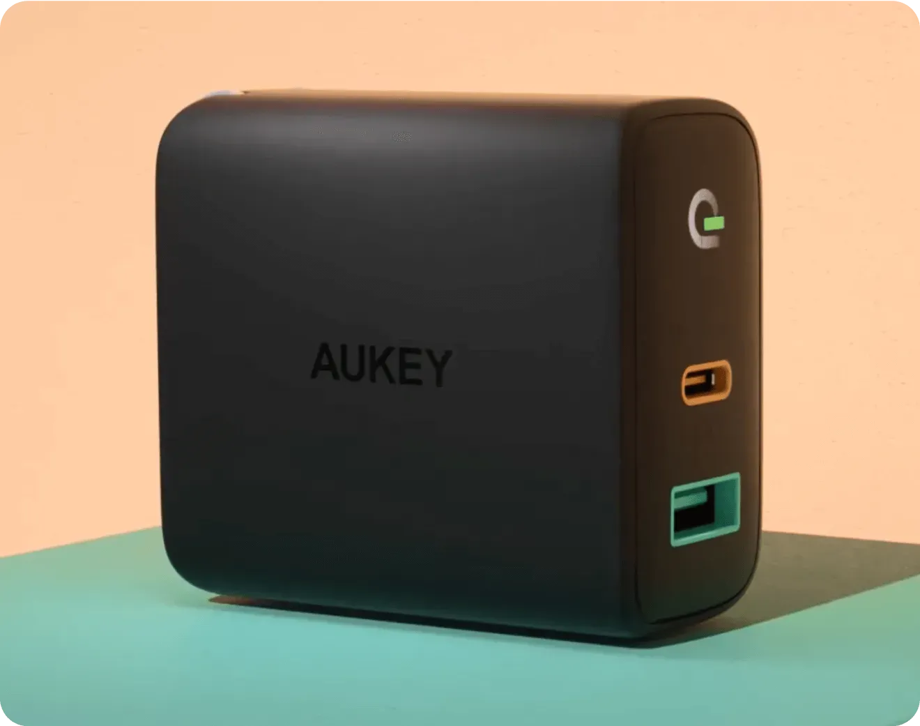 Black AUKEY USB charger with one orange USB-C port and one green USB-A port on a two-tone surface.